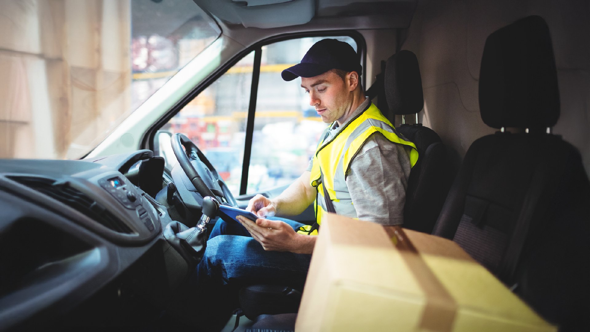 Truck driver sitting in cab using a mobile check in app with a package next to him.